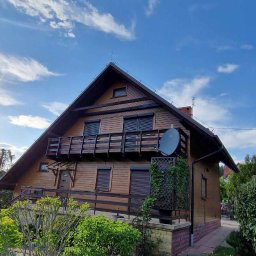 Haratyk - Drewniany dom z balkonem, brązową elewacją i satelitą na ścianie, otoczony zielenią w słoneczny dzień.