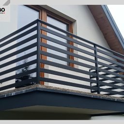 WBO Oskar Winowiecki - Nowoczesna, czarna, pozioma konstrukcja na balkonie z widocznym oknem i fragmentem dachu budynku w tle. Minimalistyczny design.