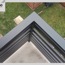 WBO Oskar Winowiecki - Nowoczesna, grafitowa balustrada balkonowa z metalowymi, poziomymi szczeblami, widziana z góry. Tło stanowi trawnik i fragment drewnianego ogrodzenia.