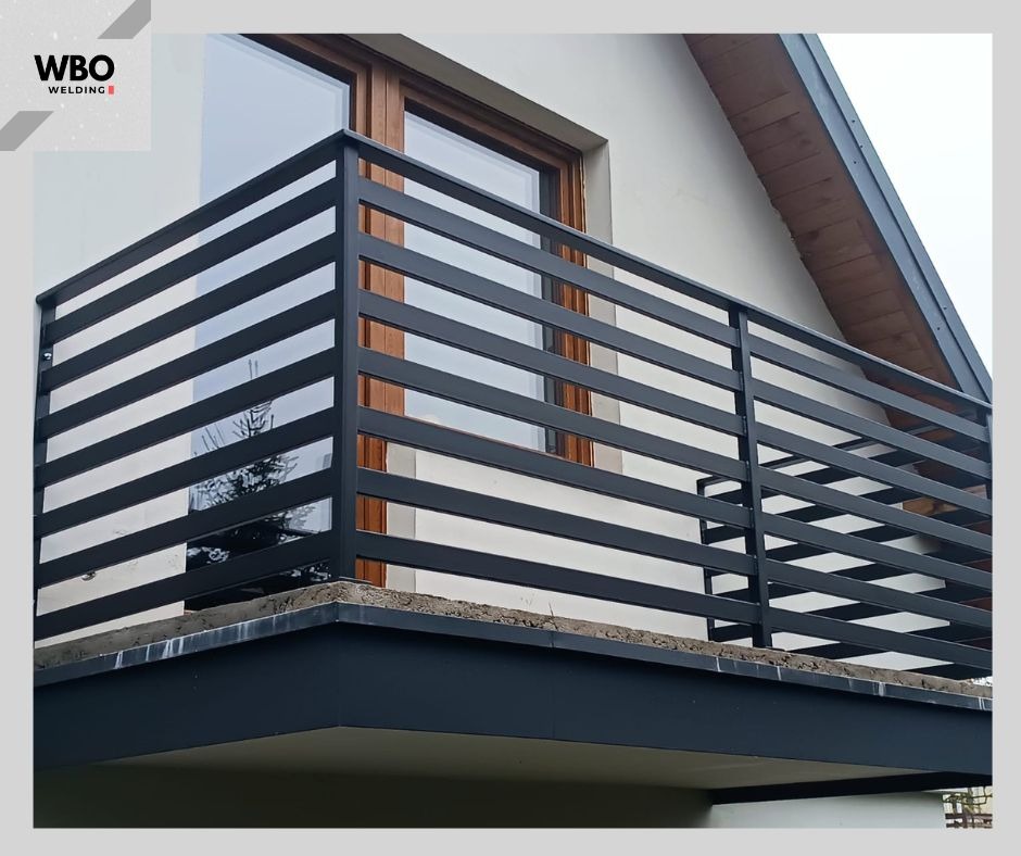 Nowoczesna, czarna, pozioma konstrukcja na balkonie z widocznym oknem i fragmentem dachu budynku w tle. Minimalistyczny design.