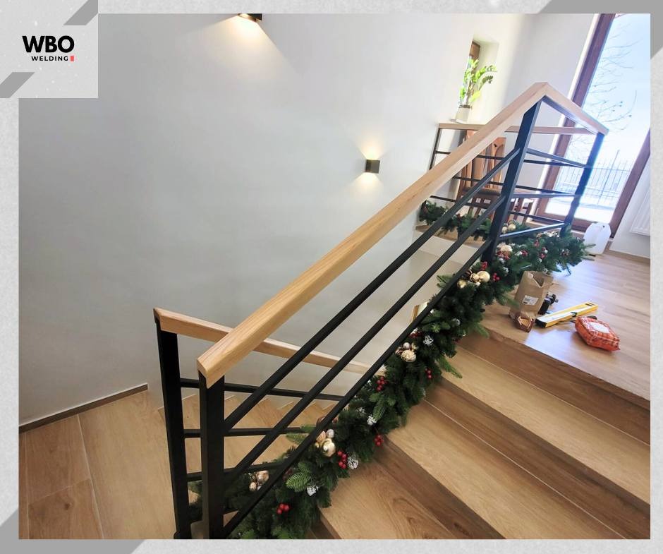 Nowoczesne schody z czarną, metalową konstrukcją i drewnianą poręczą, udekorowane świąteczną girlandą. Widok z góry, oświetlenie punktowe.