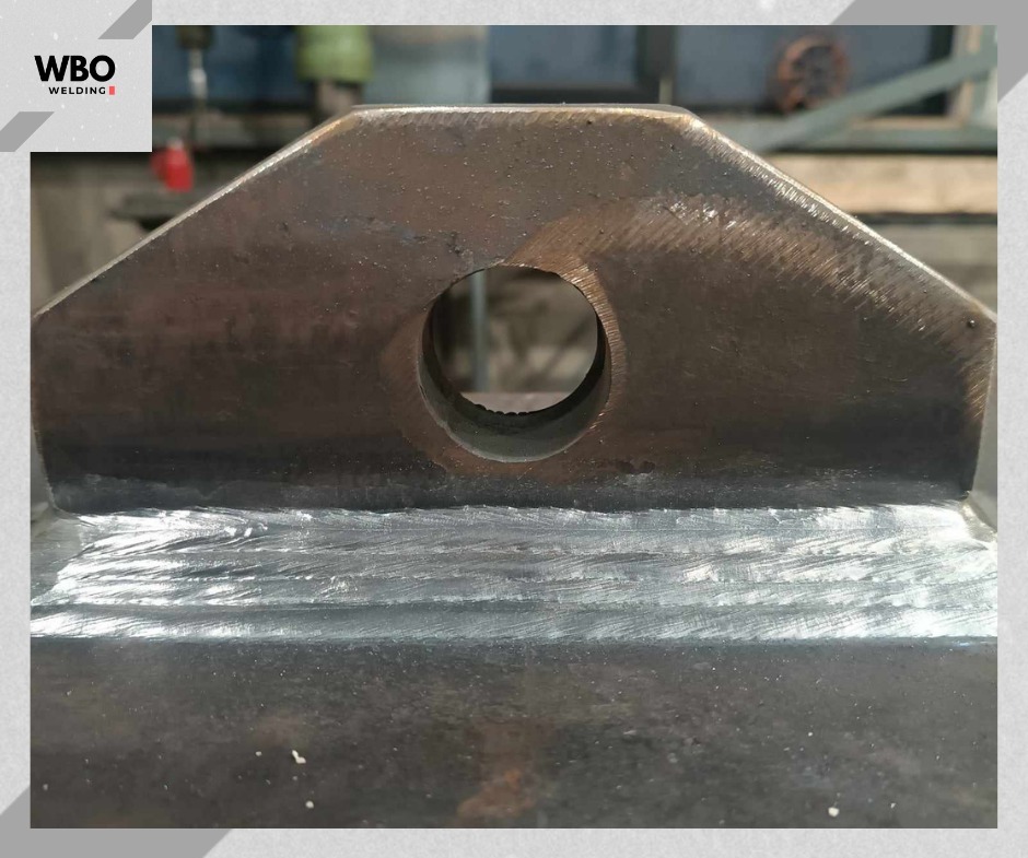 Spoina spawalnicza na grubym, metalowym elemencie z otworem. Widoczne ślady obróbki i charakterystyczny wygląd spoiny. Detal konstrukcyjny po spawaniu.