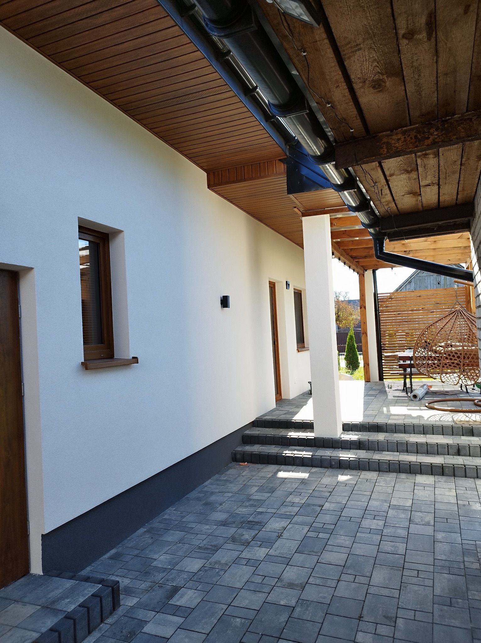 Wykończona elewacja domu z widocznym ociepleniem fundamentów, szarym brukiem na podwórku i drewnianym podbitką dachu.