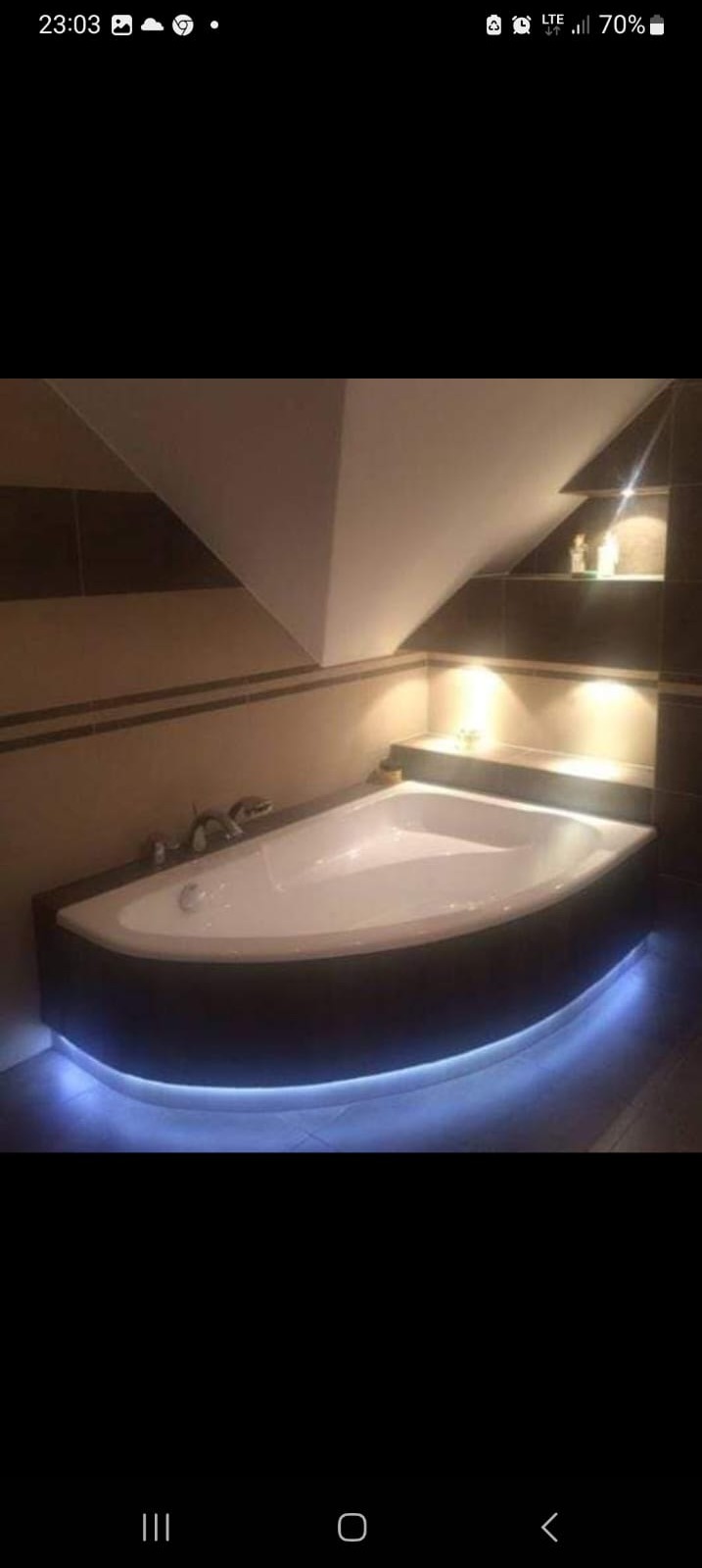 Nowoczesna łazienka na poddaszu z narożną wanną z podświetleniem LED, beżowe płytki i półki wnękowe z oświetleniem punktowym.