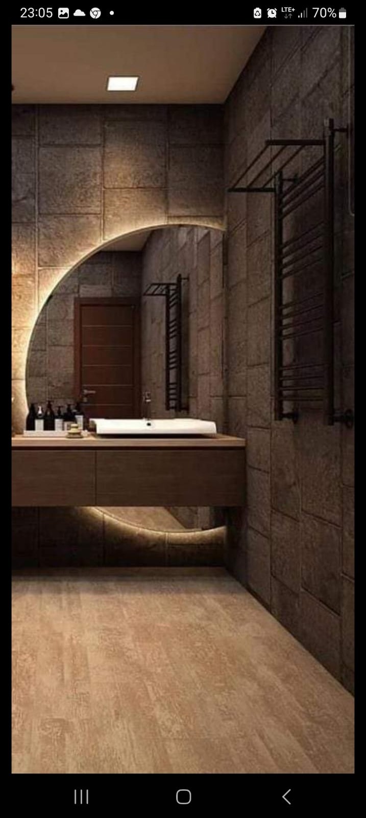 Nowoczesna łazienka z oświetlonym lustrem w kształcie półkola, ciemnymi płytkami imitującymi kamień, drewnianą szafką pod umywalką z podświetleniem LED i grzejnikiem drabinkowym.