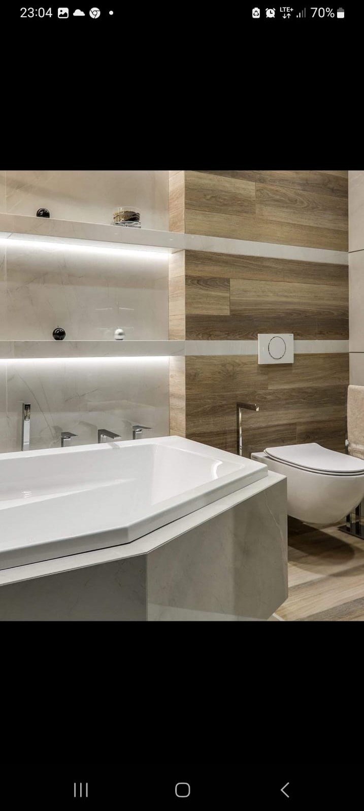 Nowoczesna łazienka z wanną o nietypowym kształcie, drewnopodobnymi płytkami na ścianie i podświetlanymi półkami.