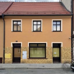 PRZEDSIĘBIORSTWO OGÓLNOBUDOWLANE KOZBUD SPÓŁKA Z OGRANICZONĄ ODPOWIEDZIALNOŚCIĄ - Odnowiona elewacja kamienicy z pomarańczową fasadą, trzema oknami na górze i jednym dużym oknem na dole, z numerem 35 nad wejściem i elementami dekoracyjnymi z imitacji kamienia na dole.