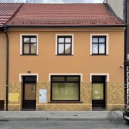 Odnowiona elewacja kamienicy z pomarańczową fasadą, trzema oknami na górze i jednym dużym oknem na dole, z numerem 35 nad wejściem i elementami dekoracyjnymi z imitacji kamienia na dole.