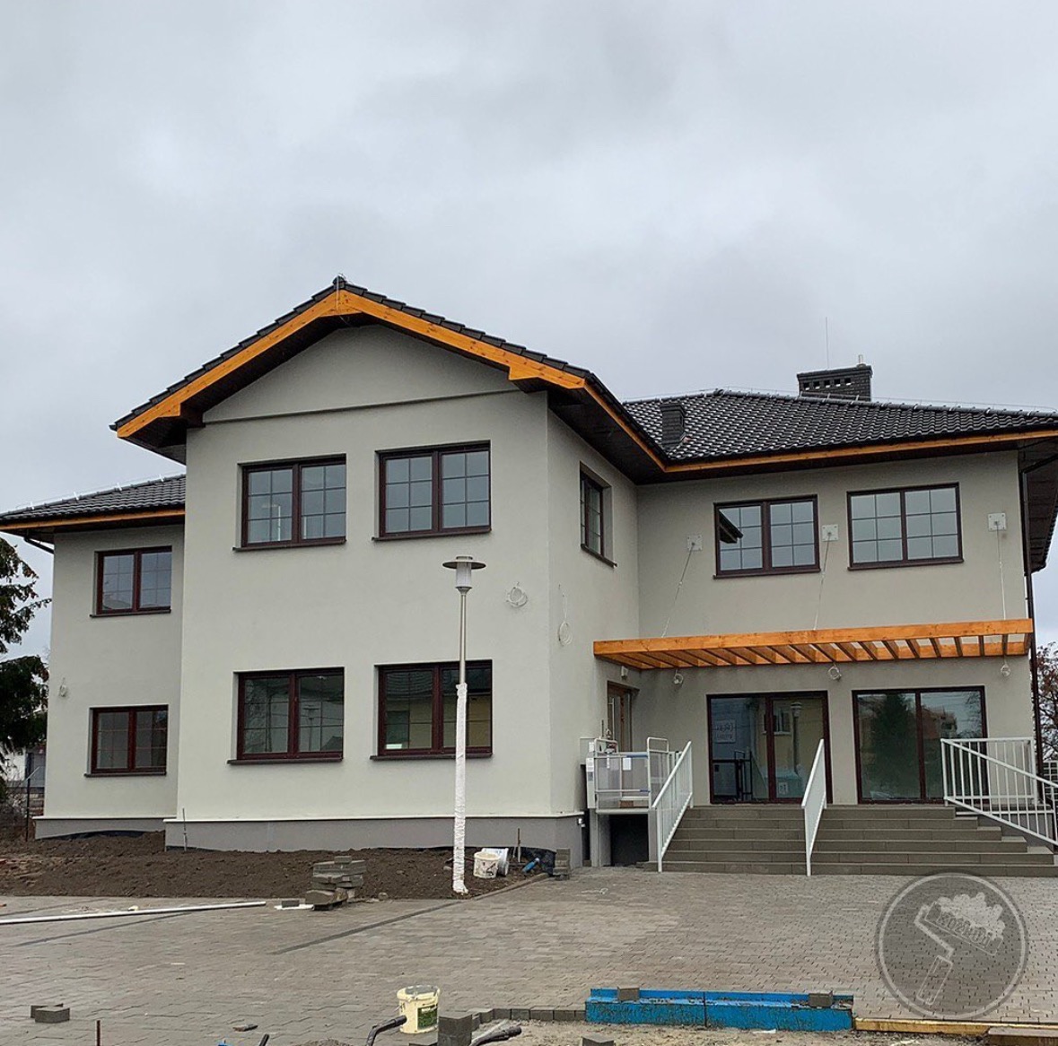 Dwupiętrowy dom po remoncie elewacji w odcieniach szarości z ciemnobrązowymi ramami okiennymi i drewnianymi elementami wykończeniowymi dachu oraz zadaszenia nad wejściem, widoczny z poziomu...