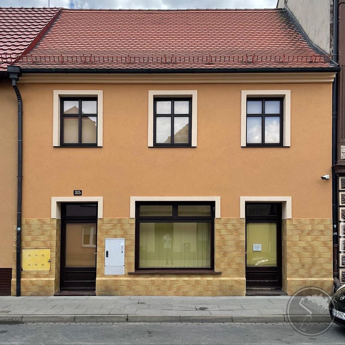 Odnowiona elewacja kamienicy z pomarańczową fasadą, trzema oknami na górze i jednym dużym oknem na dole, z numerem 35 nad wejściem i elementami dekoracyjnymi z imitacji kamienia na dole.