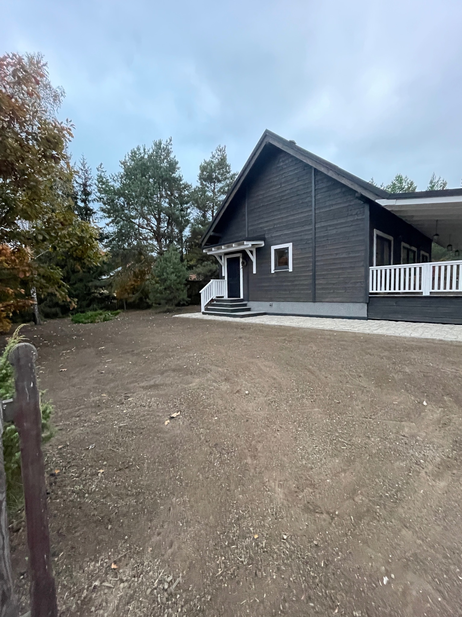 Przygotowany teren pod trawnik przed nowoczesnym, ciemnym domem z białymi elementami wykończeniowymi, widok na uprawioną ziemię i fragment ogrodzenia.