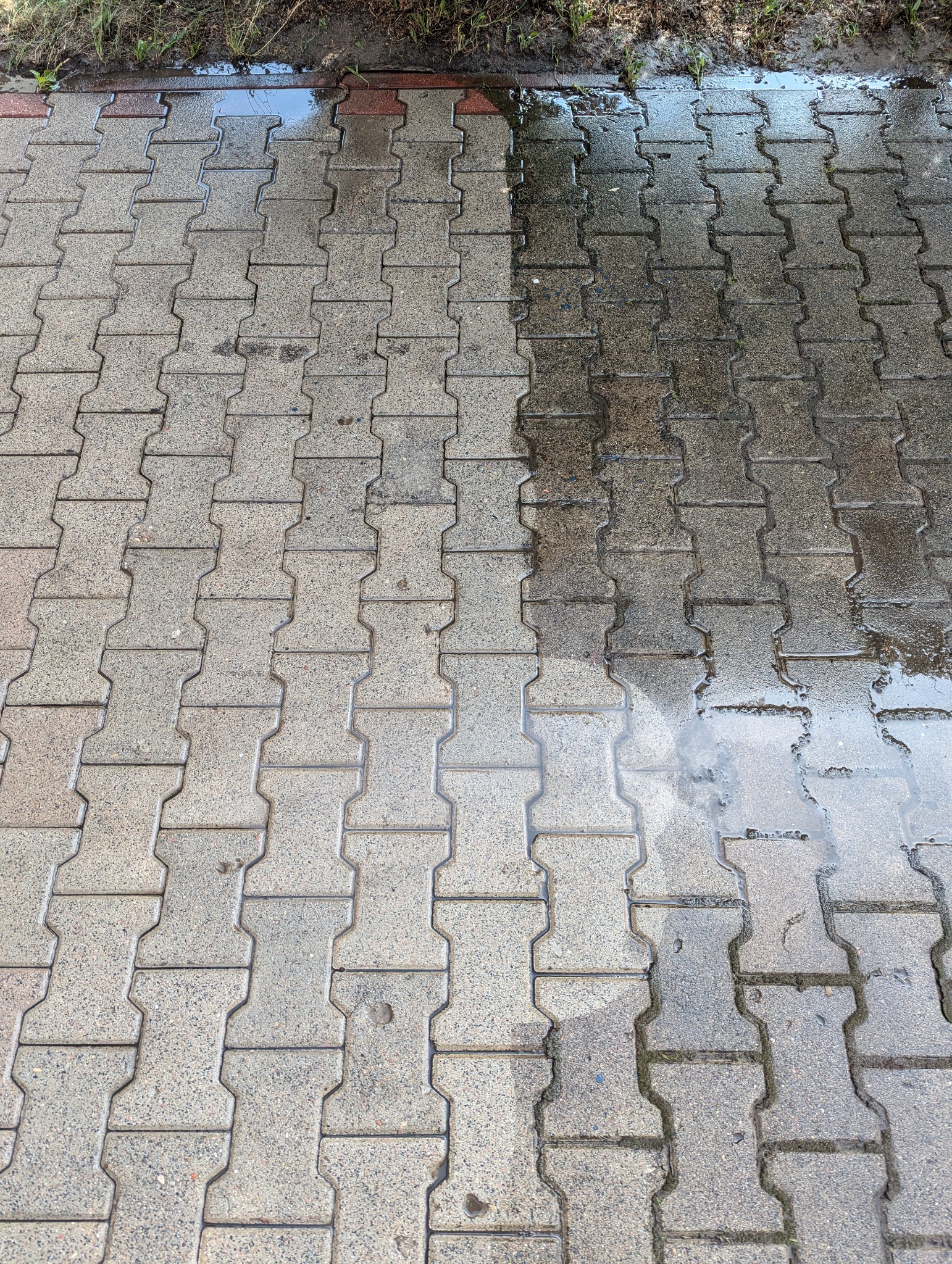 Częściowo umyta kostka brukowa w kształcie litery H, widoczna różnica w kolorze między czystą a brudną powierzchnią, mokra nawierzchnia.