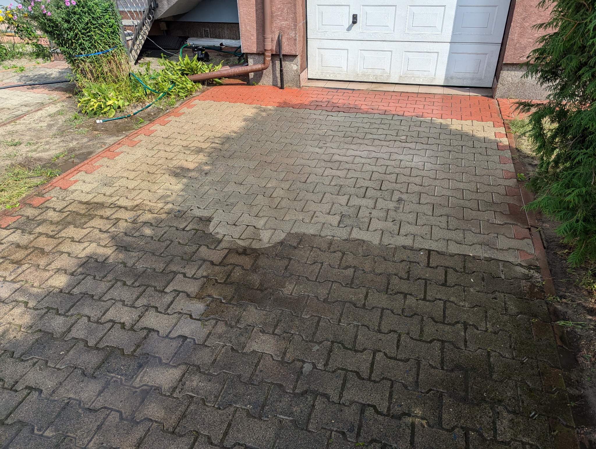 Częściowo umyta kostka brukowa przed garażem, widoczna różnica w kolorze między czystą a brudną powierzchnią.