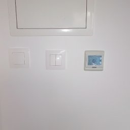 MAPKIM remonty - Biała ściana z klapą rewizyjną, pojedynczym i podwójnym włącznikiem światła oraz termostatem pokazującym temperaturę 20.5 stopni Celsjusza.