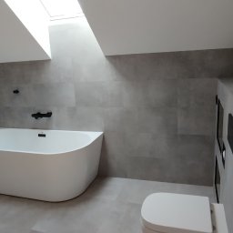 MAPKIM remonty - Nowoczesna łazienka na poddaszu z wolnostojącą białą wanną, szarą glazurą, drewnopodobną ścianą w jodełkę, czarną armaturą i oknem dachowym.