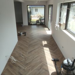 MAPKIM remonty - Ułożona podłoga z paneli w jodełkę w jasnym wnętrzu w Sosnowcu, widoczne narzędzia i sprzęt do sprzątania, przygotowane kable do montażu oświetlenia.