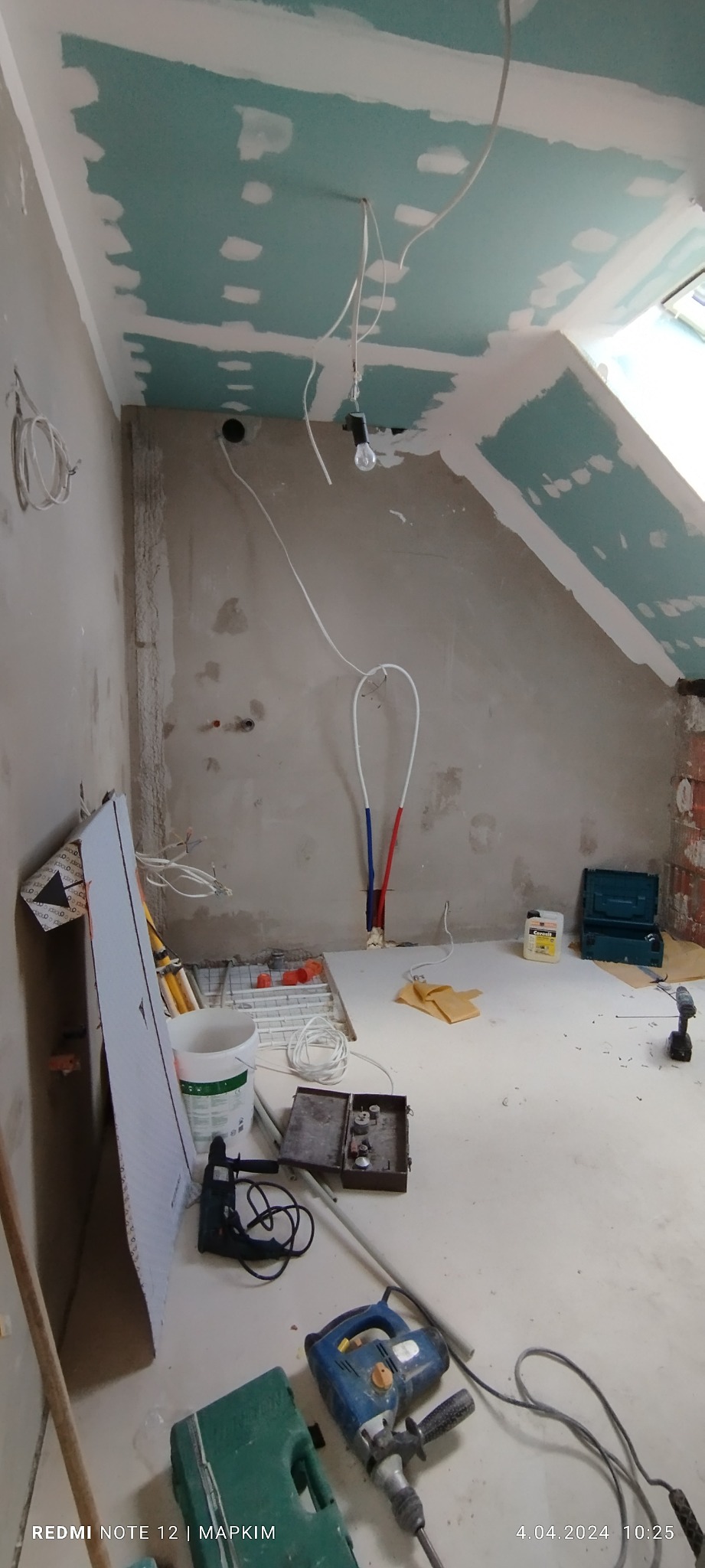 Niedokończony remont poddasza: ściany i sufit z płyt kartonowo-gipsowych, widoczne instalacje elektryczne, rury wodne, narzędzia budowlane i materiały wykończeniowe na podłodze.