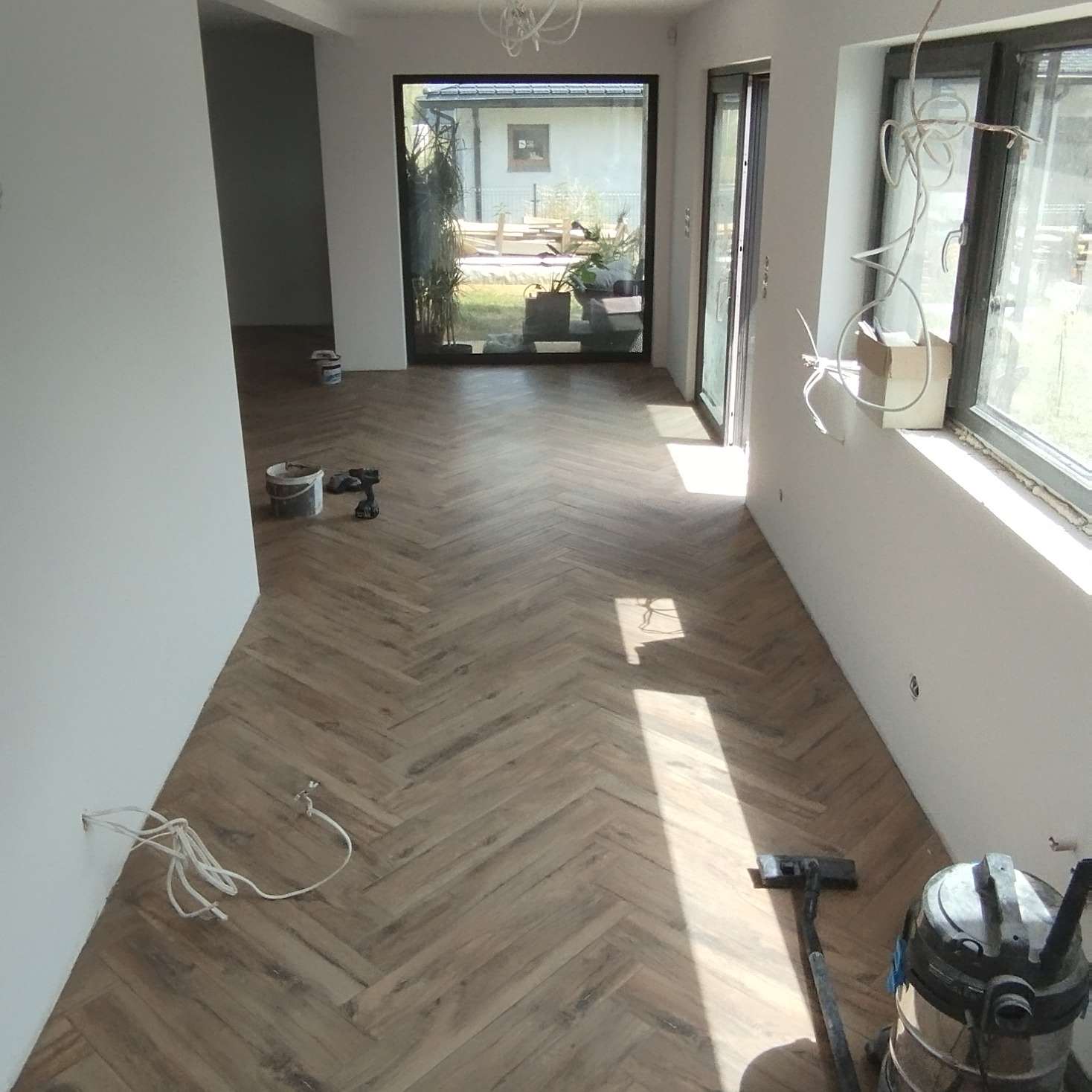 Ułożona podłoga z paneli w jodełkę w jasnym wnętrzu w Sosnowcu, widoczne narzędzia i sprzęt do sprzątania, przygotowane kable do montażu oświetlenia.