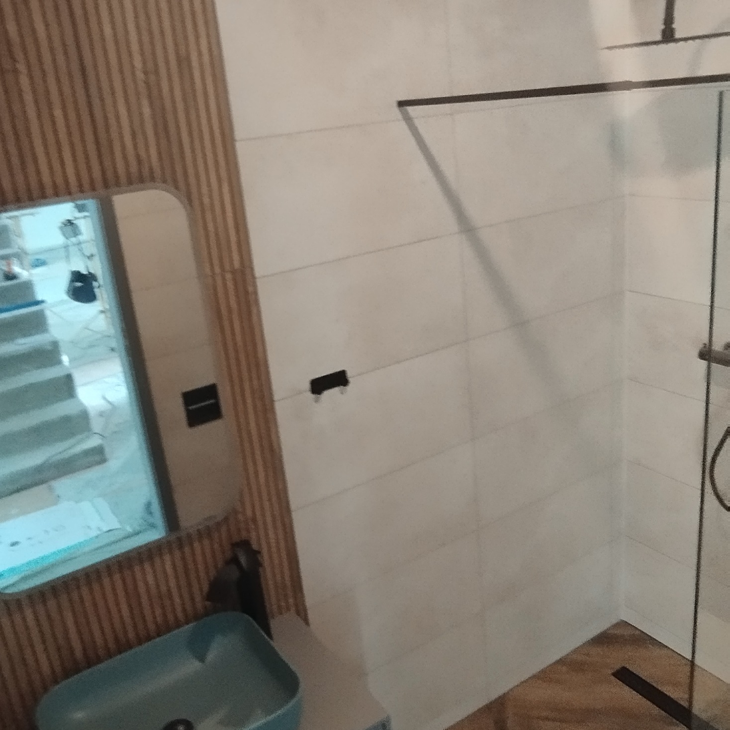 Fragment łazienki z kabiną prysznicową typu walk-in, umywalką nablatową w kolorze turkusowym oraz lustrem, w którym odbija się remontowany pokój.