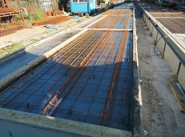 Przygotowanie formy zbrojeniowej do wylewania betonu na placu budowy. Widoczne stalowe pręty zbrojeniowe ułożone w siatkę wewnątrz formy, czekające na zalanie betonem.