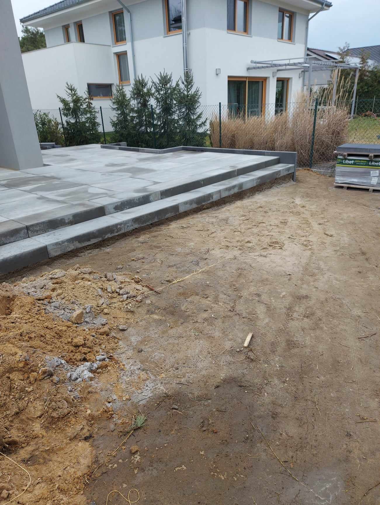 Układanie kostki brukowej w trakcie prac: widoczne ułożone schody z kostki, paleta z kostką Libet w tle, wykopana ziemia i przygotowany teren pod dalszą część nawierzchni.