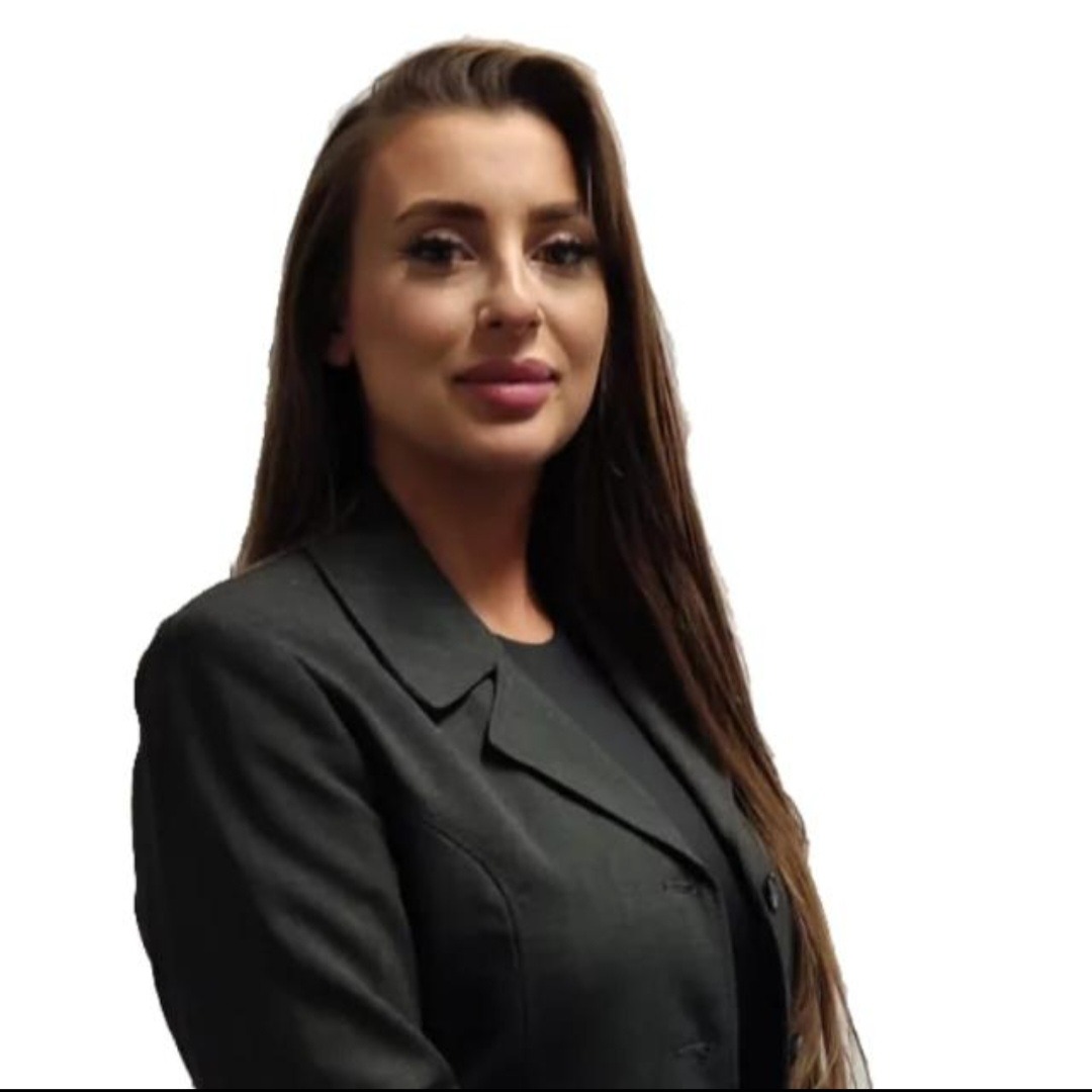 Portret kobiety w czarnej marynarce, z długimi brązowymi włosami, prezentującej profesjonalny wizerunek w jasnym otoczeniu.