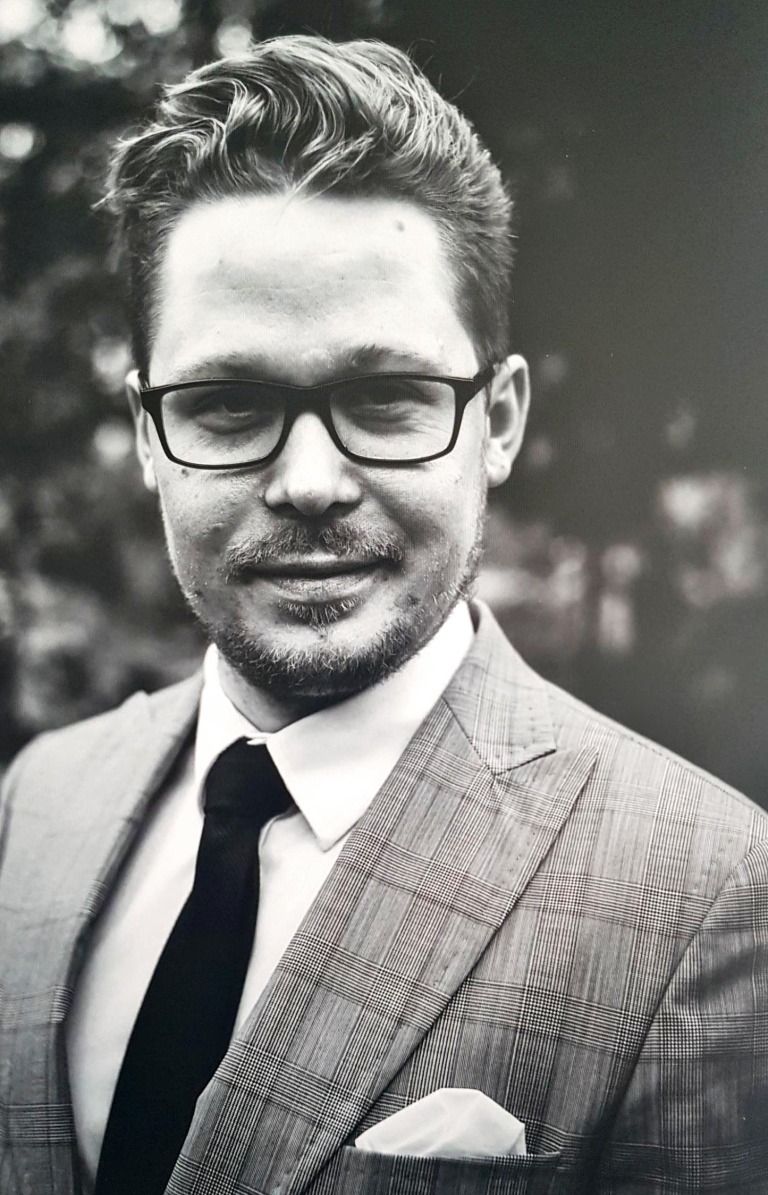 Portret biznesowy mężczyzny w okularach, w garniturze w kratę, z poszetką w kieszonce, czarno-białe zdjęcie.