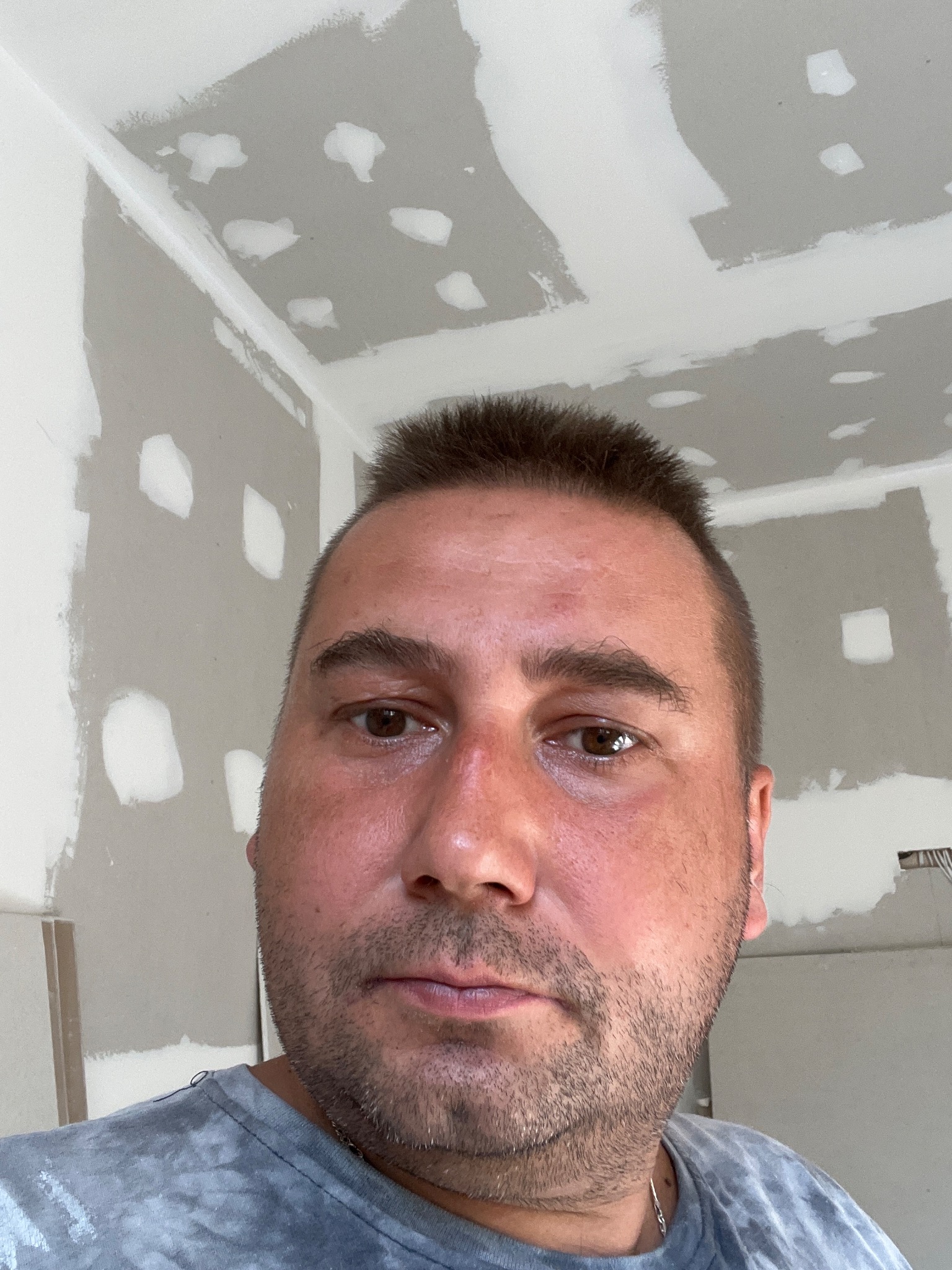 Mężczyzna w trakcie szpachlowania sufitu, widoczne ślady szpachli na suficie i ścianie, zarys instalacji elektrycznej.