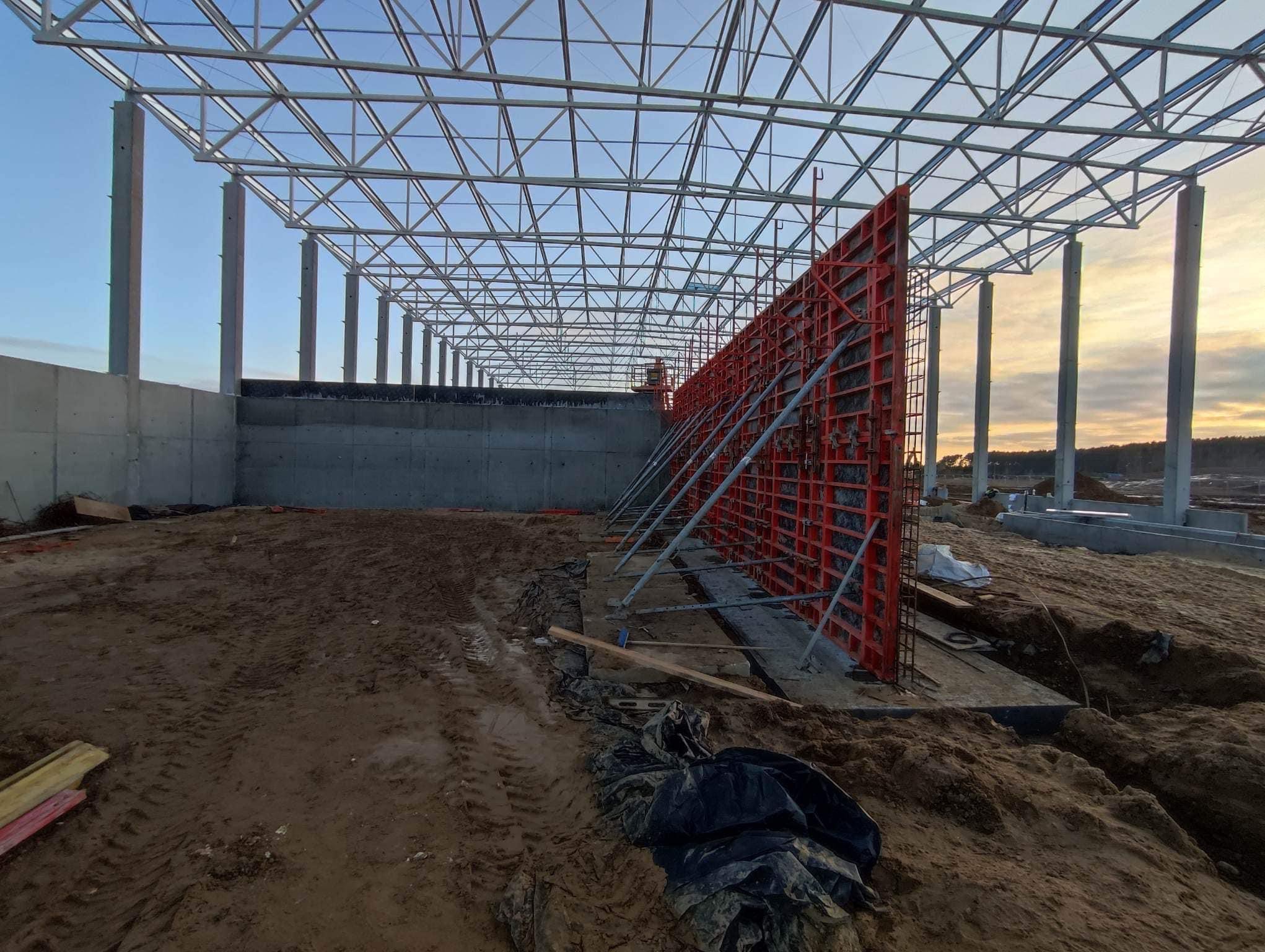 Konstrukcja szalunku wewnątrz budowanego budynku żelbetowego, widoczne stalowe podpory, słupy konstrukcyjne i zarys nieba w tle.