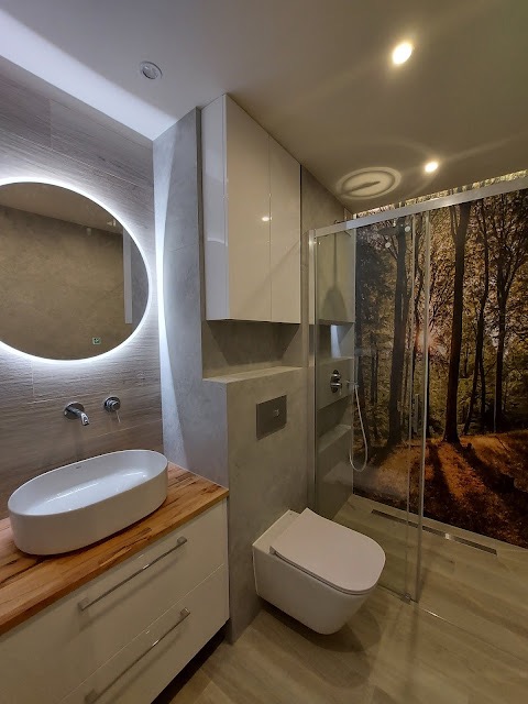 Nowoczesna łazienka z owalną umywalką nablatową na drewnianym blacie, podświetlanym lustrem, wiszącą toaletą i kabiną prysznicową z fototapetą leśną.