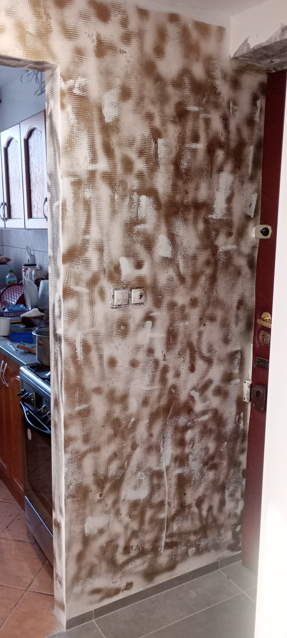 Przygotowanie ściany w kuchni do malowania: siatka wzmacniająca zatopiona w zaprawie, widoczne puszki instalacyjne, fragment zabudowy kuchennej.