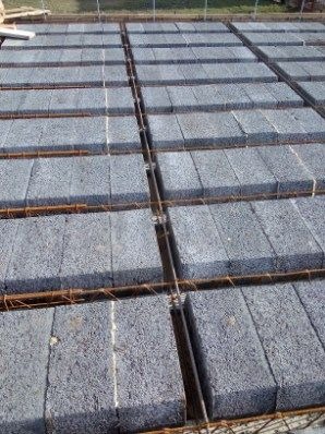 Szare bloczki betonowe ułożone na fundamencie z wystającymi prętami zbrojeniowymi, przygotowane do zalania betonem.