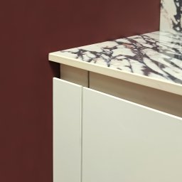 Art Room Studio Natalia Fierka - Fragment blatu kuchennego z marmurowym wzorem i białymi frontami szafek na tle bordowej ściany.