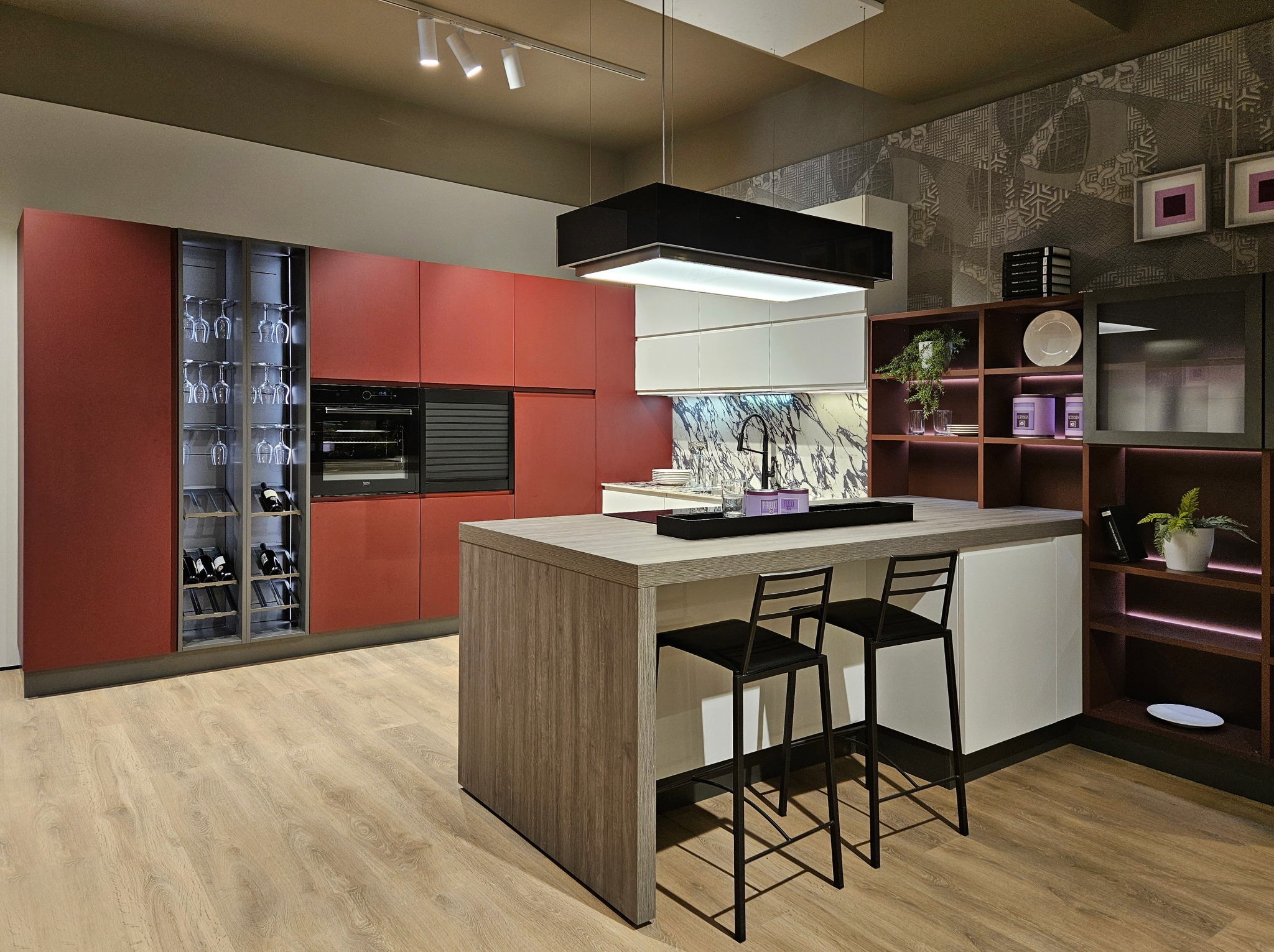Nowoczesna kuchnia z czerwonymi szafkami, wyspą z drewnianym blatem i czarnymi hokerami, oświetleniem podszafkowym i marmurowym backsplashiem.