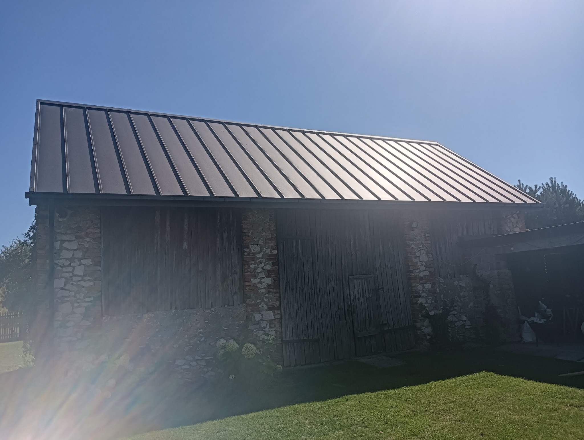 Metalowy dach trapezowy na budynku gospodarczym w Ostrowach nad Okszą, widok z dołu, błękitne niebo w tle. Nowoczesne krycie dachu.