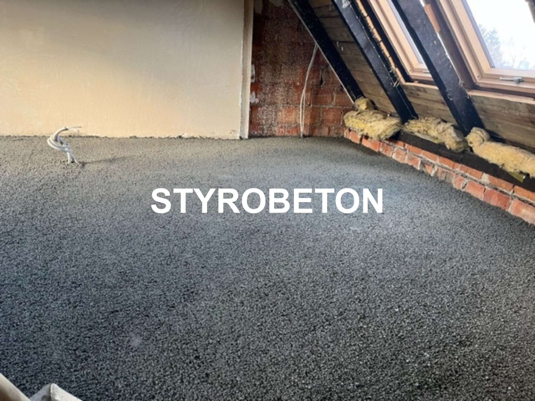 Szara, świeżo wylana posadzka w surowym wnętrzu poddasza z widoczną izolacją i fragmentem instalacji elektrycznej.