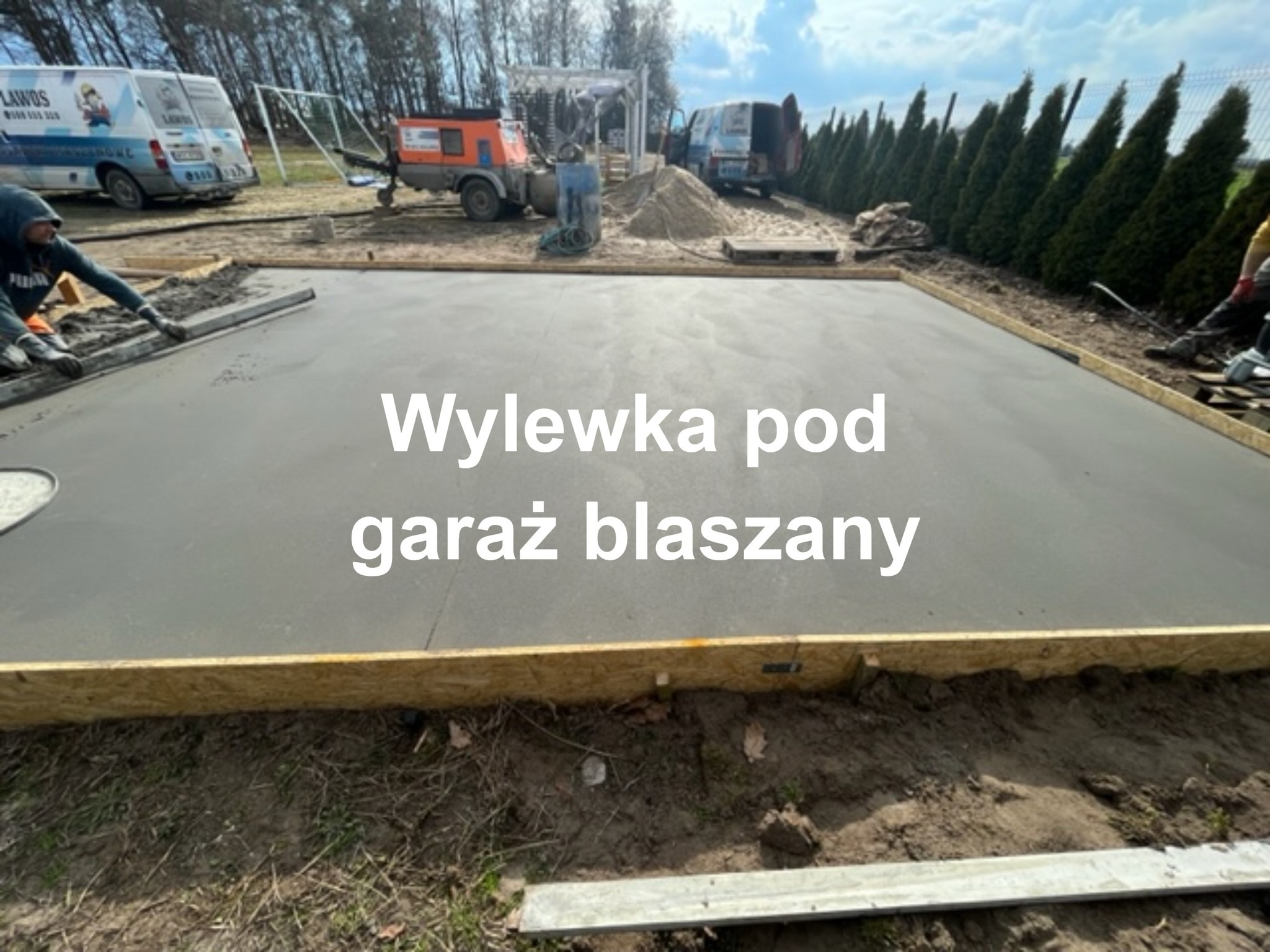 Świeżo wylana, gładka płyta betonowa pod garaż blaszany, otoczona drewnianym szalunkiem, z widocznymi pracownikami i sprzętem budowlanym w tle.