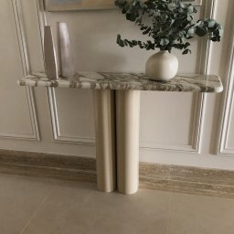 Konsola z kamiennym blatem oraz metalowymi nogami lakierowanymi w połysk.