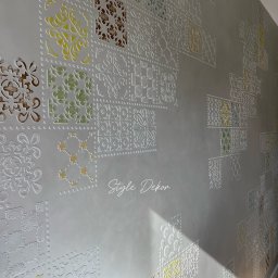 STYLE DEKOR Oksana Nahurna - Dekoracyjna ściana z wypukłymi, białymi wzorami w stylu marokańskim na szarym tle, z subtelnymi kolorowymi wstawkami żółci, zieleni i brązu.