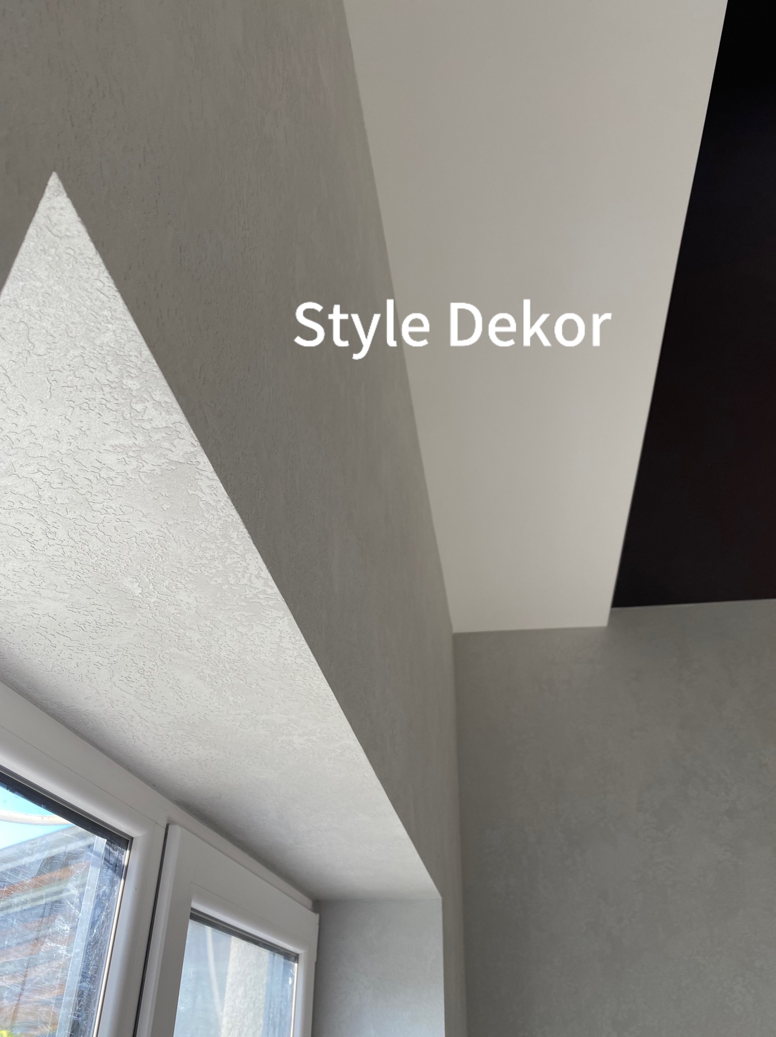 Ściana z szarą, dekoracyjną strukturą przy oknie, z białym wykończeniem sufitu i fragmentem czarnego sufitu w rogu.
