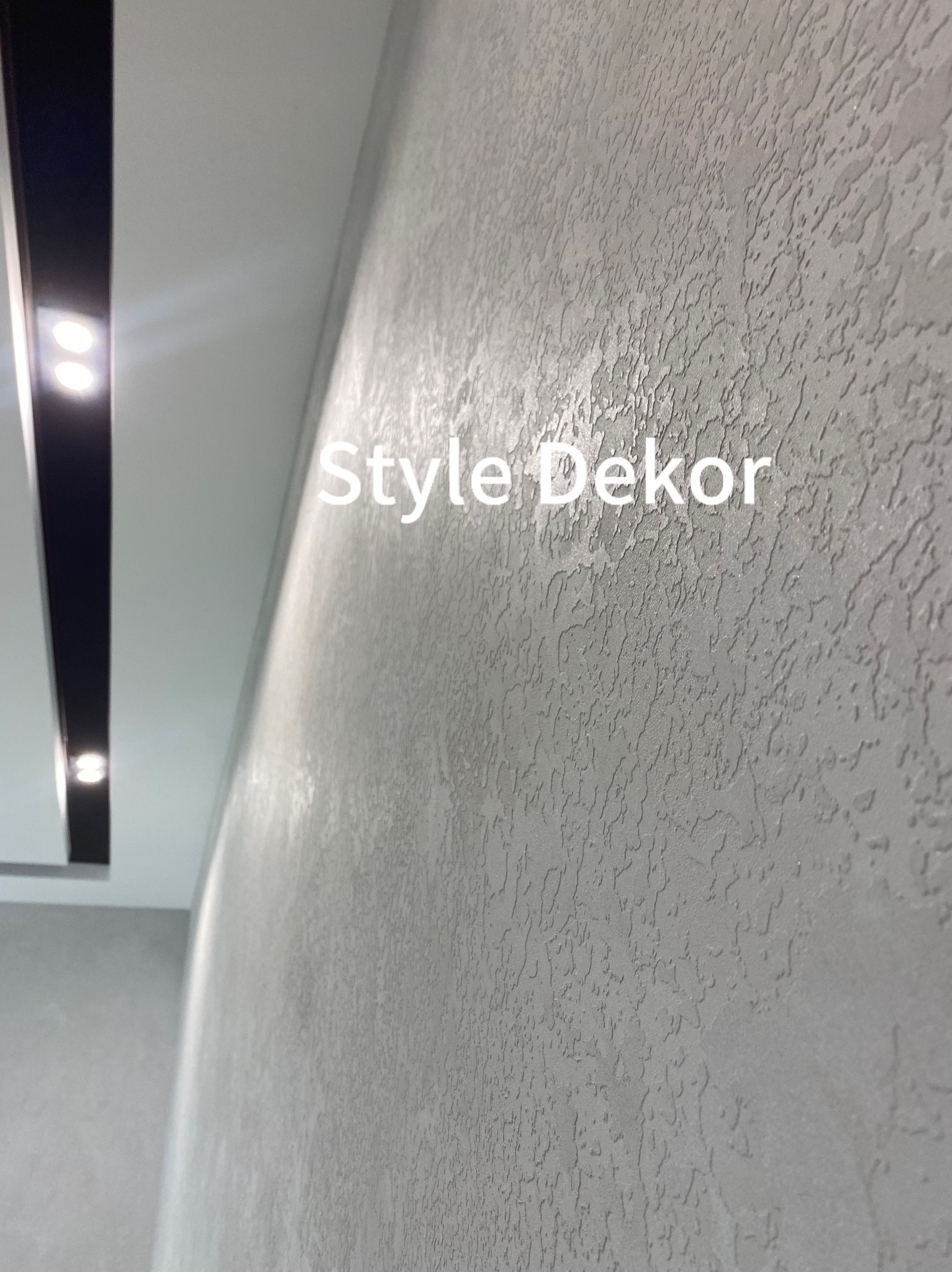Szara ściana z dekoracyjną fakturą, oświetlona listwą LED w suficie, z widocznym napisem 'Style Dekor'.