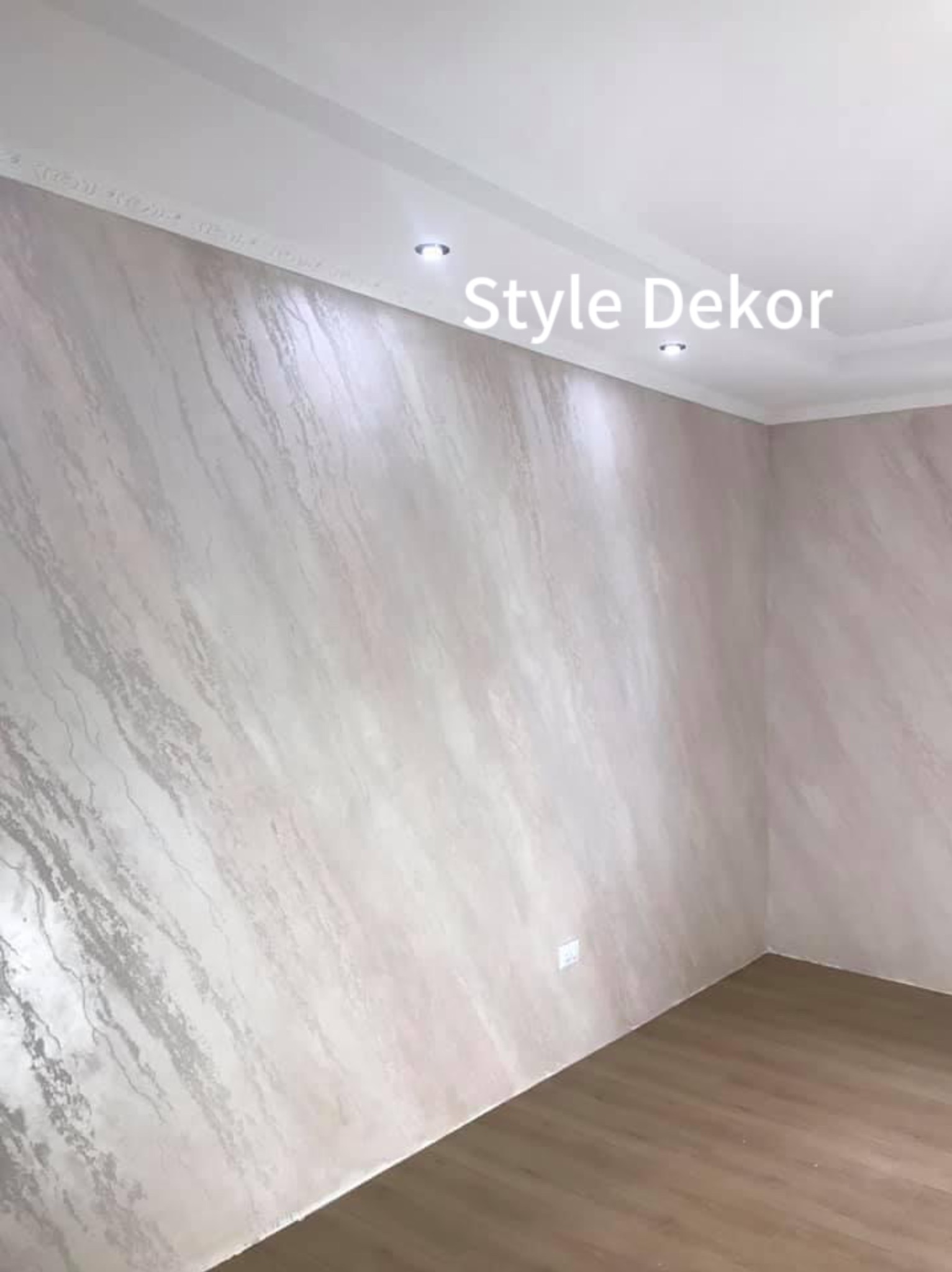 Ściana w pokoju z dekoracyjną, marmurkową strukturą, listwa przysufitowa i drewniana podłoga.