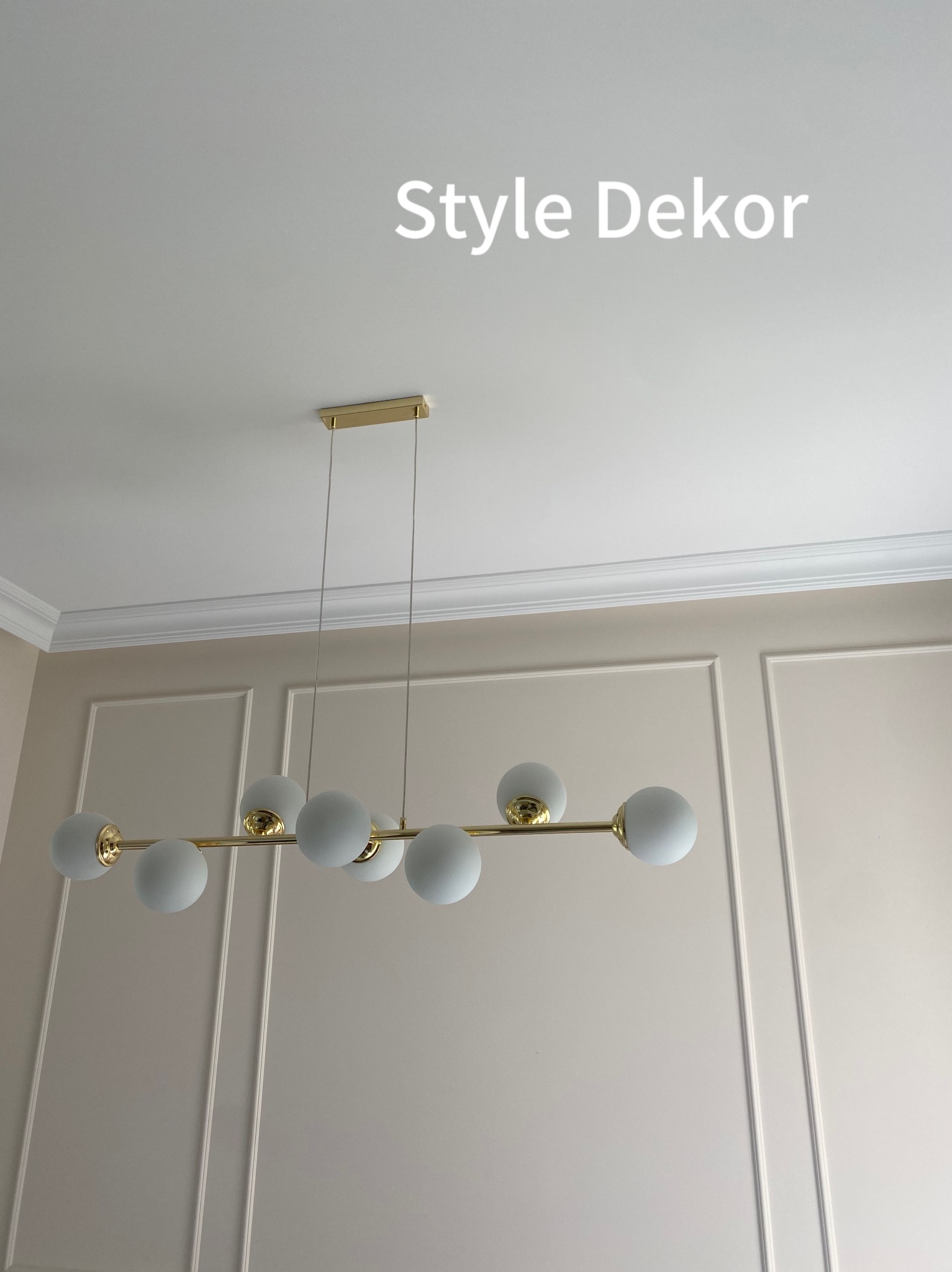 Nowoczesny żyrandol z białymi kulami i złotymi detalami zamontowany w Piasecznie na tle ściany z dekoracyjnymi listwami i gładzią.