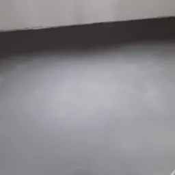 Świeżo wylana, szara wylewka samopoziomująca na podłodze, widoczne fragmenty cegły przy ścianie.