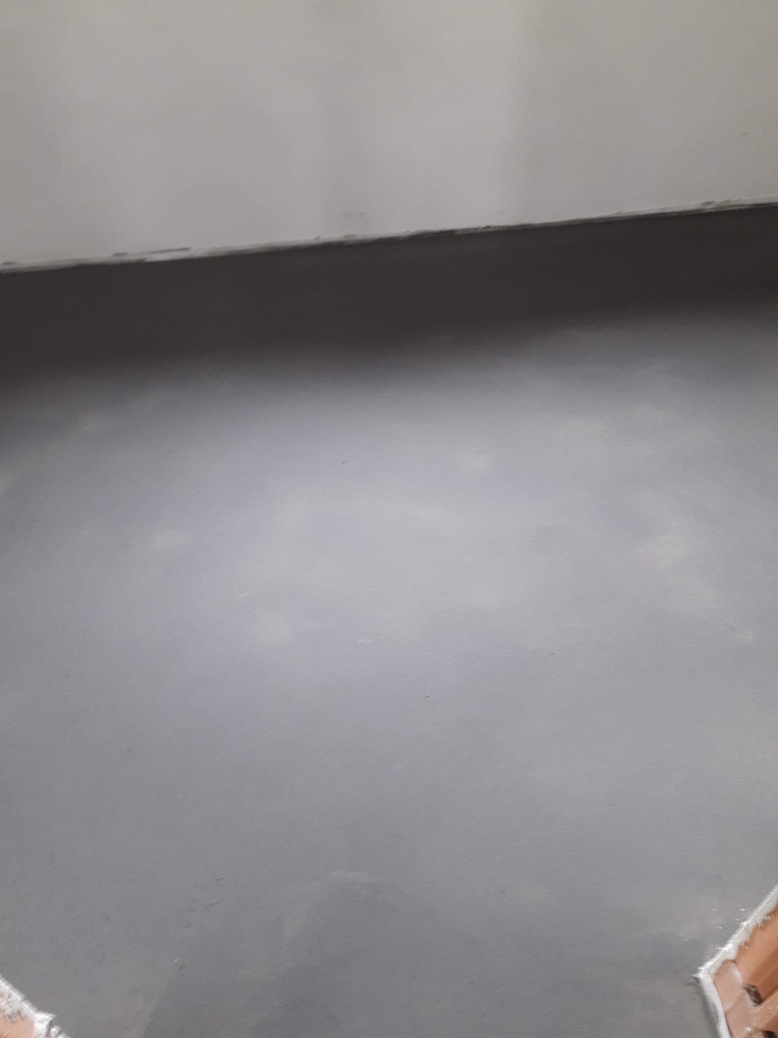 Świeżo wylana, szara wylewka samopoziomująca na podłodze, widoczne fragmenty cegły przy ścianie.