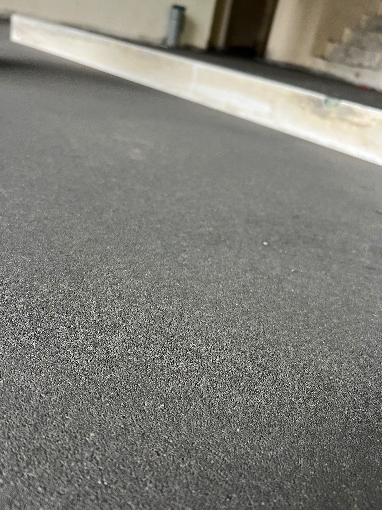 Szara, szorstka powierzchnia nowej podłogi z poziomnicą w tle, ukazująca etap prac wykończeniowych.