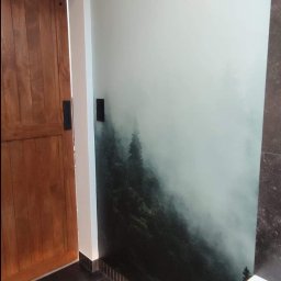 Spec Remonty - Nowoczesna łazienka z ciemną podłogą, drewnianymi drzwiami i fototapetą z motywem mglistego lasu na ścianie.