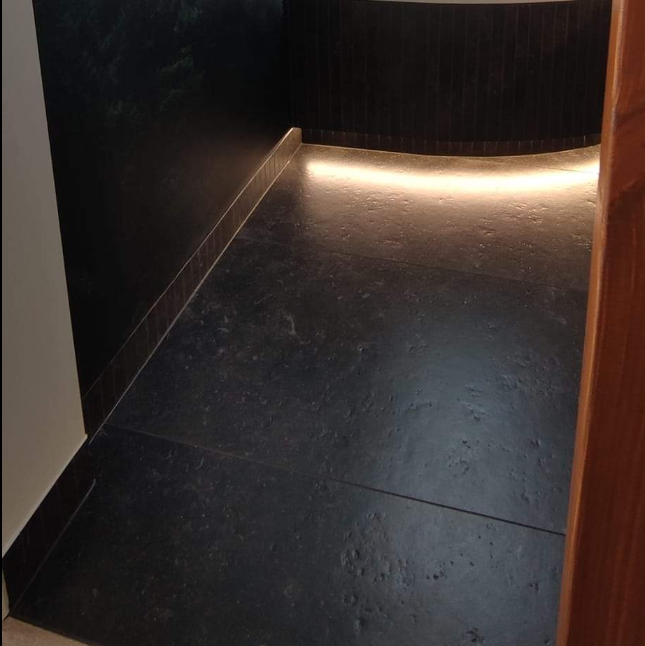 Ciemna, elegancka łazienka z podświetlaną wnęką i płytkami imitującymi kamień, widok zza framugi drzwi.