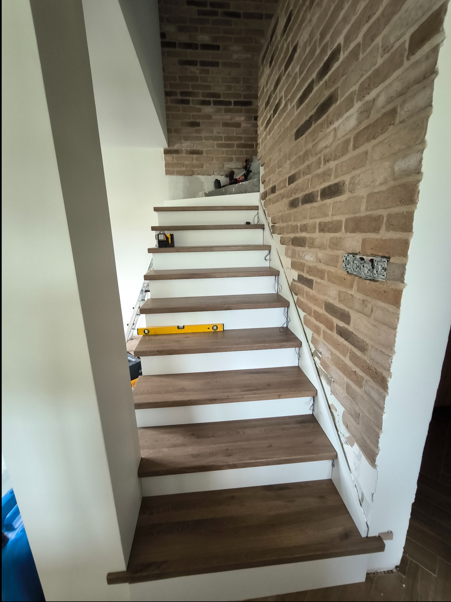 Montaż drewnopodobnych paneli na schodach w Białymstoku, widoczna ściana z cegły dekoracyjnej i narzędzia pracy.