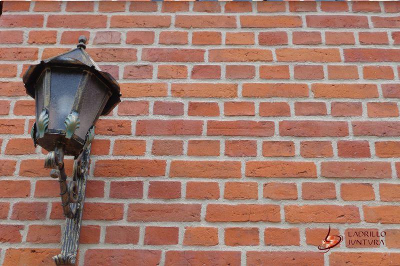 Ściana z czerwonej cegły z zamontowaną ozdobną, metalową lampą w stylu retro z motywem liści na wsporniku.